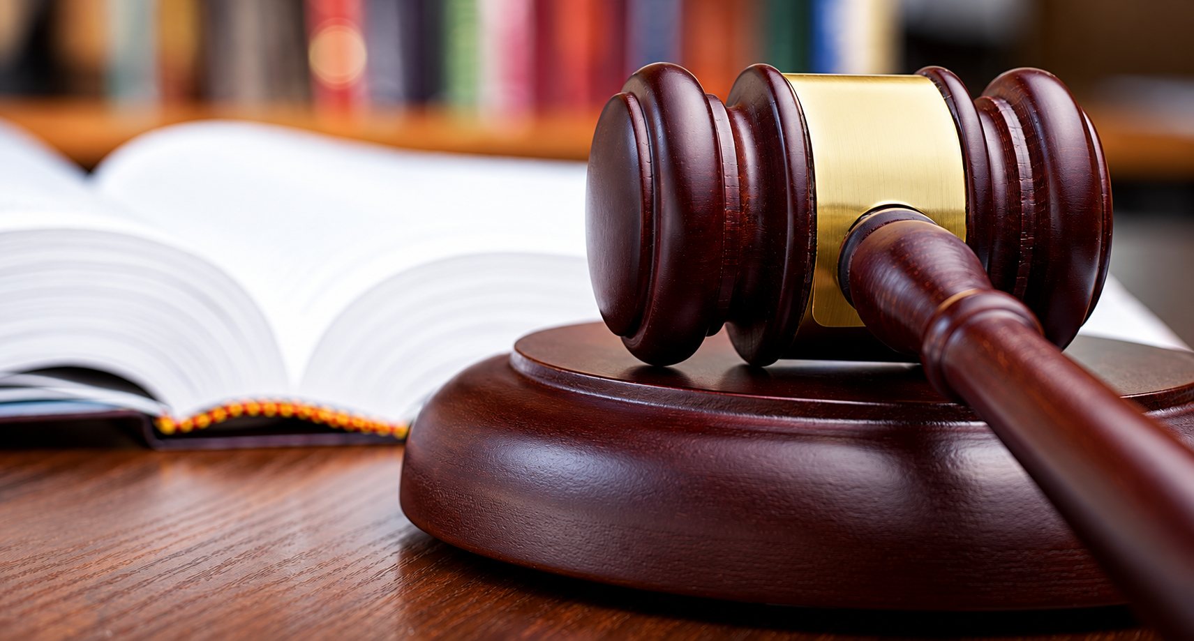 Un marteau de juge en bois sombre à bague dorée sur son socle, devant un livre de droit ouvert.
